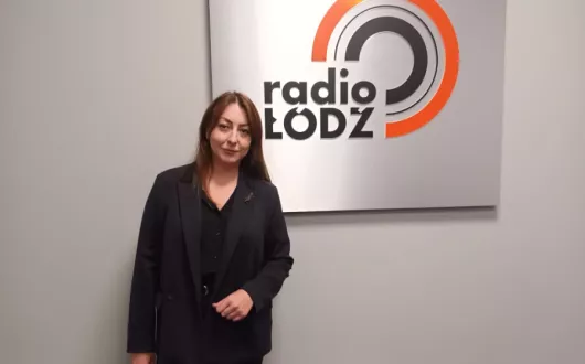 Kobieta stojąca przy ścianie, gdzie umieszczone jest logo radia Łódź