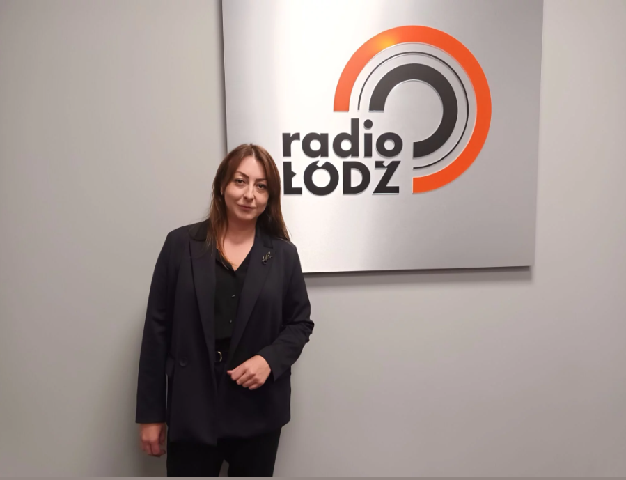 Kobieta stojąca przy ścianie, gdzie umieszczone jest logo radia Łódź